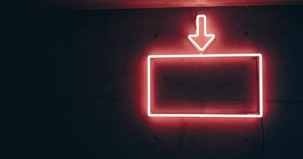 A glowing neon downward arrow above a widescreen rectangle outline on a dark wall