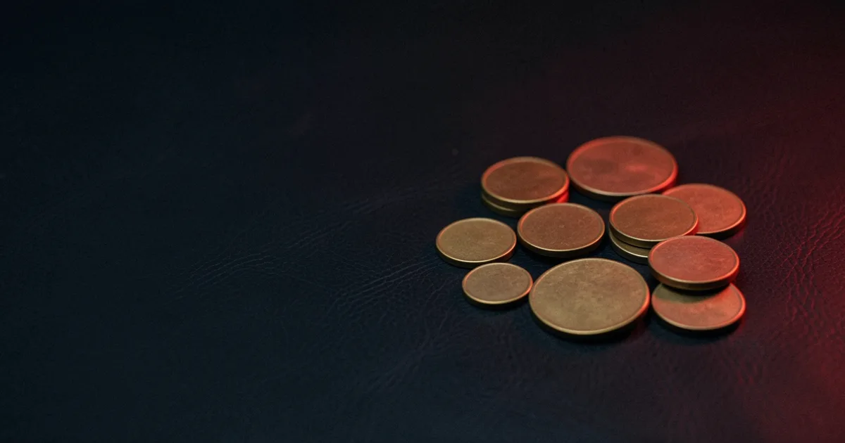 A scatter of brass coins of different sizes on dark leather under a red light