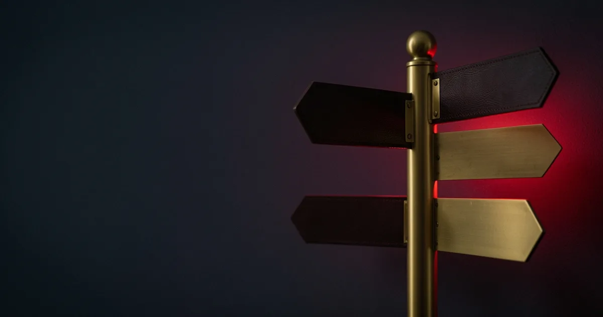A brass signpost with three blank arms pointing in different directions on dark leather under a red light