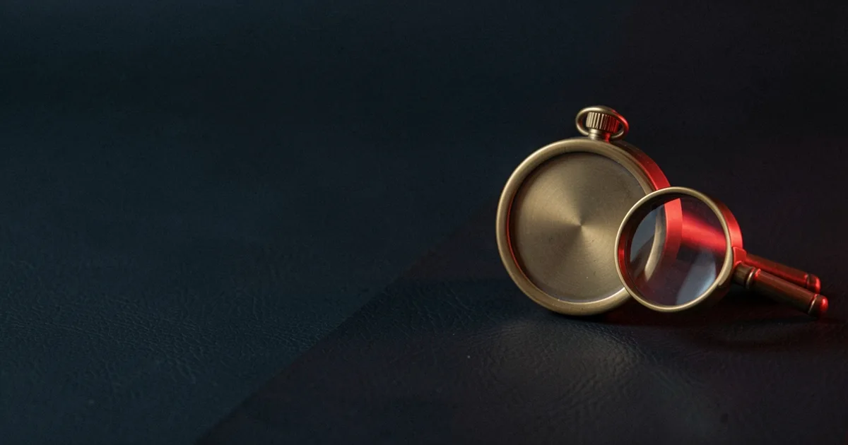 A brass gauge with a plain blank dial and a small brass magnifying glass on dark leather under a red light