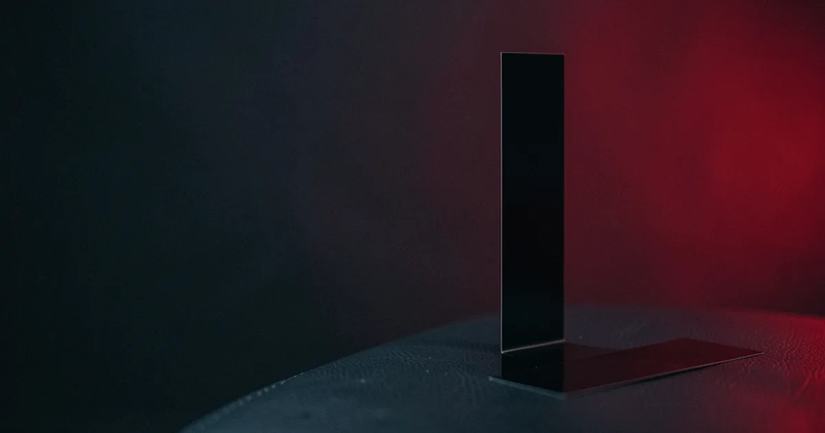 A tall black strip standing upright beside a flat black strip on dark leather under a red light
